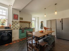 A kitchen with a wooden dining table and chairs a green stove a washing machine and a stainless steel refrigerator at Coach House Llanwrtyd Wells