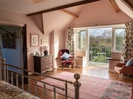 A bedroom with a metal bed frame a wooden chest of drawers an armchair and a balcony with outdoor furniture at Coach House in Llanwrtyd Wells