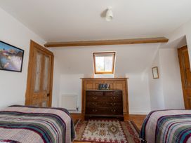 A bedroom with two beds with striped blankets a wooden dresser with books a rug a small window and wooden doors at Coach House in Llanwrtyd Wells