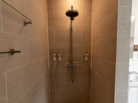 A tiled shower area with a large showerhead three dispensers and glass shelves at Coach House in Llanwrtyd Wells