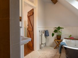 A bathroom with a bathtub a towel rail a wooden door a potted plant and a small table at Coach House in Llanwrtyd Wells