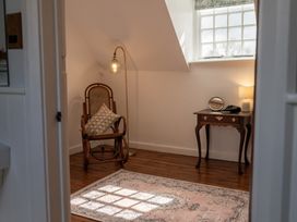 A small room with a wooden rocking chair, a pillow, a floor lamp, a wooden table with a mirror and a lamp, and a patterned rug on the floor at Coach House in Llanwrtyd Wells