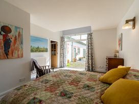 A bedroom with a patterned bedspread yellow pillows wooden chair paintings on walls and curtains open to a garden at Coach House in Llanwrtyd Wells
