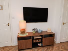 A wall-mounted television above a wooden cabinet with a lamp plant decor candles and books in a room at Coastal Retreat in Seahouses