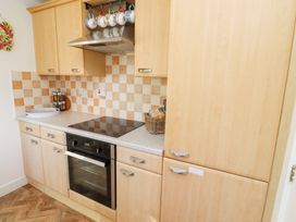 A kitchen with wooden cabinets an electric stove oven and a basket with bread at Coastal Retreat in Seahouses