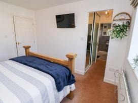 A bedroom with a wooden bed frame a mounted TV a door and an entrance to a bathroom at Coastal Retreat in Seahouses