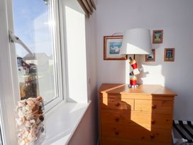 A window with a vase of seashells on the sill next to a wooden chest of drawers with a lamp and framed pictures on the wall at Coastal Retreat in Seahouses