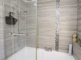 A bathroom with a bathtub shower and tiled walls at Coastal Retreat in Seahouses