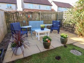 A backyard patio with blue and light blue wooden chairs a white table and several potted plants at Coastal Retreat in Seahouses