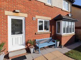 The exterior of a red brick house with a white door blue bench and potted plants at Coastal Retreat in Seahouses