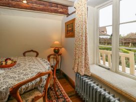 A dining area with a round table covered by a patterned tablecloth surrounded by wooden chairs a lamp on a side table a window with curtains and a radiator below at Thatch Cottage in Trunch