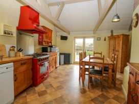 A kitchen with wooden cabinets a red stove and a wooden dining table with chairs at Thatch Cottage in Trunch