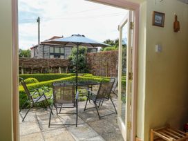View of a garden patio with four chairs around a table and an umbrella seen from inside a room at Thatch Cottage in Trunch