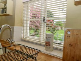 A kitchen sink area with a dish rack cutting board and a ceramic container on a windowsill at Thatch Cottage in Trunch