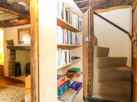 A bookshelf with books and board games next to carpeted stairs and a fireplace in a living area at Thatch Cottage in Trunch