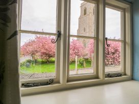 A window view showing pink blossoming trees and a church tower at Thatch Cottage in Trunch