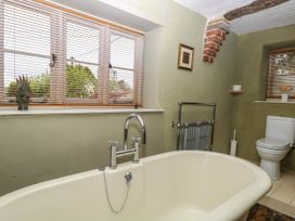 A bathroom with a bathtub sink toilet radiator and windows with blinds at Thatch Cottage in Trunch