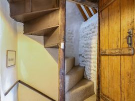 A narrow staircase with carpeted steps and a wooden door with stone walls at Thatch Cottage in Trunch