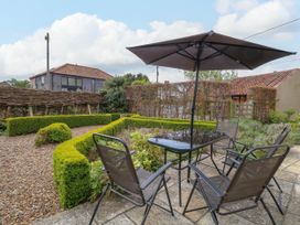 An outdoor patio with a table umbrella and four chairs next to a garden with low hedges at Thatch Cottage in Trunch