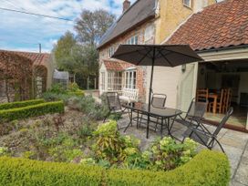 A patio with table chairs and umbrella next to a garden and a thatched cottage at Thatch Cottage in Trunch