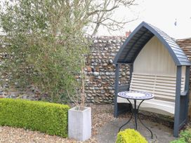 A garden area with a covered bench and round mosaic table near a stone wall at Thatch Cottage in Trunch
