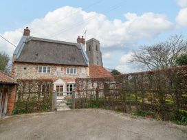 A thatched roof cottage with a wooden gate and trimmed hedge in front at Thatch Cottage in Trunch