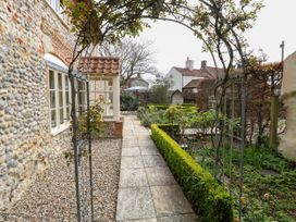 A garden walkway with an arch trellis leading to a seating area by a stone house at Thatch Cottage in Trunch