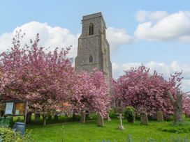 A stone church tower surrounded by pink blossom trees and tombstones at Thatch Cottage in Trunch