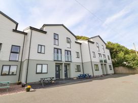 A row of three-story modern townhouses with picnic tables and flower pots outside at 3 Yr Hen Lys in Pwllheli