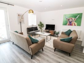 A living room with two brown sofas a gray chair a white coffee table a floor lamp a television on a wooden stand and a colorful painting of a bull at 3 Yr Hen Lys in Pwllheli