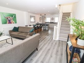 An open plan living room with two sofas a dining table with chairs a kitchen island stools and a staircase at 3 Yr Hen Lys in Pwllheli