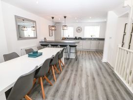 A kitchen and dining area with a long white table and grey chairs at 3 Yr Hen Lys in Pwllheli