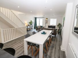 A dining area with a white table and eight chairs next to a living space with two sofas and a TV at 3 Yr Hen Lys in Pwllheli