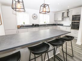 A kitchen with a large island, three black bar stools, hanging light fixtures, white cabinets, and black countertop at 3 Yr Hen Lys in Pwllheli
