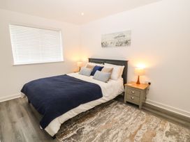 A bedroom with a bed with navy blanket and pillows bedside tables with lamps a window with blinds and a rug on the floor at 3 Yr Hen Lys in Pwllheli