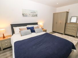A bedroom with a bed a nightstand with a lamp a wardrobe a chest of drawers and a painting on the wall at 3 Yr Hen Lys in Pwllheli