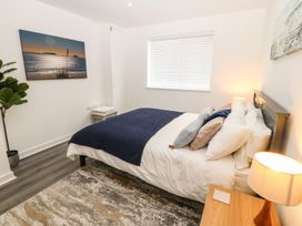A bedroom with a bed covered with pillows and a blanket a bedside table with a lamp a window with blinds a plant a wall painting and a stool with towels at 3 Yr Hen Lys in Pwllheli
