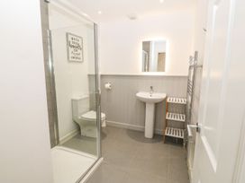 A bathroom with a shower, toilet, sink, mirror, towel rack and three-tier storage shelf at 3 Yr Hen Lys in Pwllheli