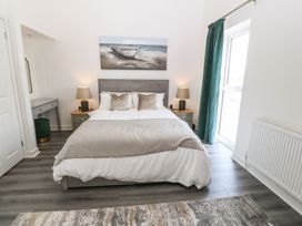 A bedroom with a double bed two bedside tables with lamps a painting of a boat on the wall and a window with green curtains at 3 Yr Hen Lys in Pwllheli