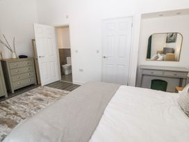 A bedroom with a bed a dresser a vanity with a mirror a rug and a door leading to a bathroom at 3 Yr Hen Lys in Pwllheli