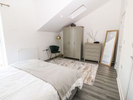 A bedroom with a bed a green chair a wardrobe a chest of drawers a floor mirror and a floor lamp at 3 Yr Hen Lys in Pwllheli