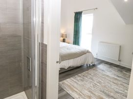 A bedroom with a bed a nightstand with lamp a window with curtain a radiator a rug and a shower visible through a doorway at 3 Yr Hen Lys in Pwllheli