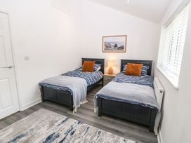A bedroom with two single beds with blue striped bedding and orange pillows a bedside table with a lamp and a framed picture on the wall at 3 Yr Hen Lys in Pwllheli