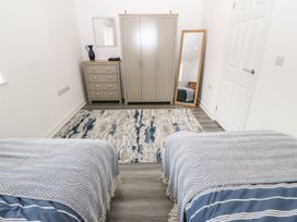 A bedroom with two beds a wardrobe a chest of drawers a standing mirror and a rug at 3 Yr Hen Lys in Pwllheli