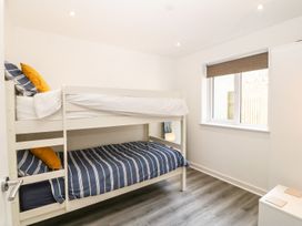 A bedroom with a white bunk bed and striped bedding a window and a small white cabinet at 3 Yr Hen Lys in Pwllheli