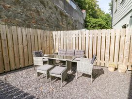 An outdoor seating area with a glass table and wicker chairs on a stone ground with a wooden fence in the background at 3 Yr Hen Lys in Pwllheli