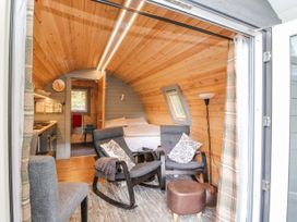 A small wooden pod interior with two gray rocking chairs, a bed, a kitchen area, and a floor lamp at Elleric Pods - The Last Resort Fasnacloich near Appin