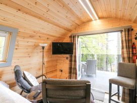 A small living area with wooden walls a chair a stool a wall mounted tv and a balcony with outdoor seating at Elleric Pods - The Last Resort in Fasnacloich near Appin