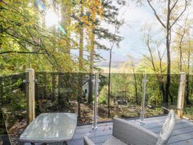 A wooden deck with glass railing chairs and a table overlooking a forest with a house in the background at Elleric Pods - The Last Resort Fasnacloich near Appin