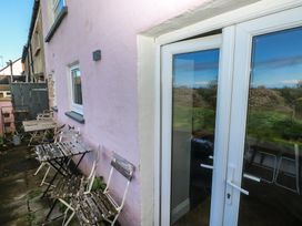 An outdoor patio area with weathered wooden tables and chairs next to a pink wall with windows and white framed glass doors at Min-Y-Ffordd in Dinas Cross